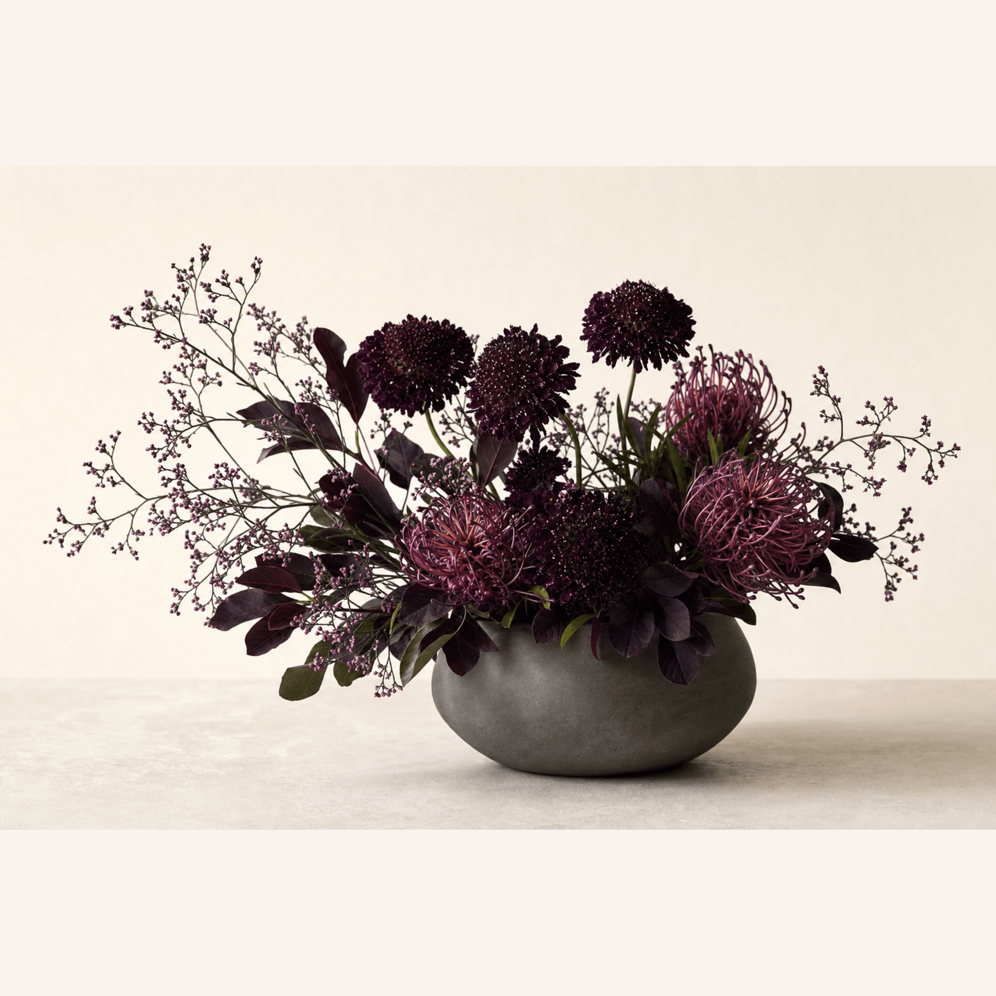 Deep purple scabiosa and pincushion protea with limonium in a grey stone bowl