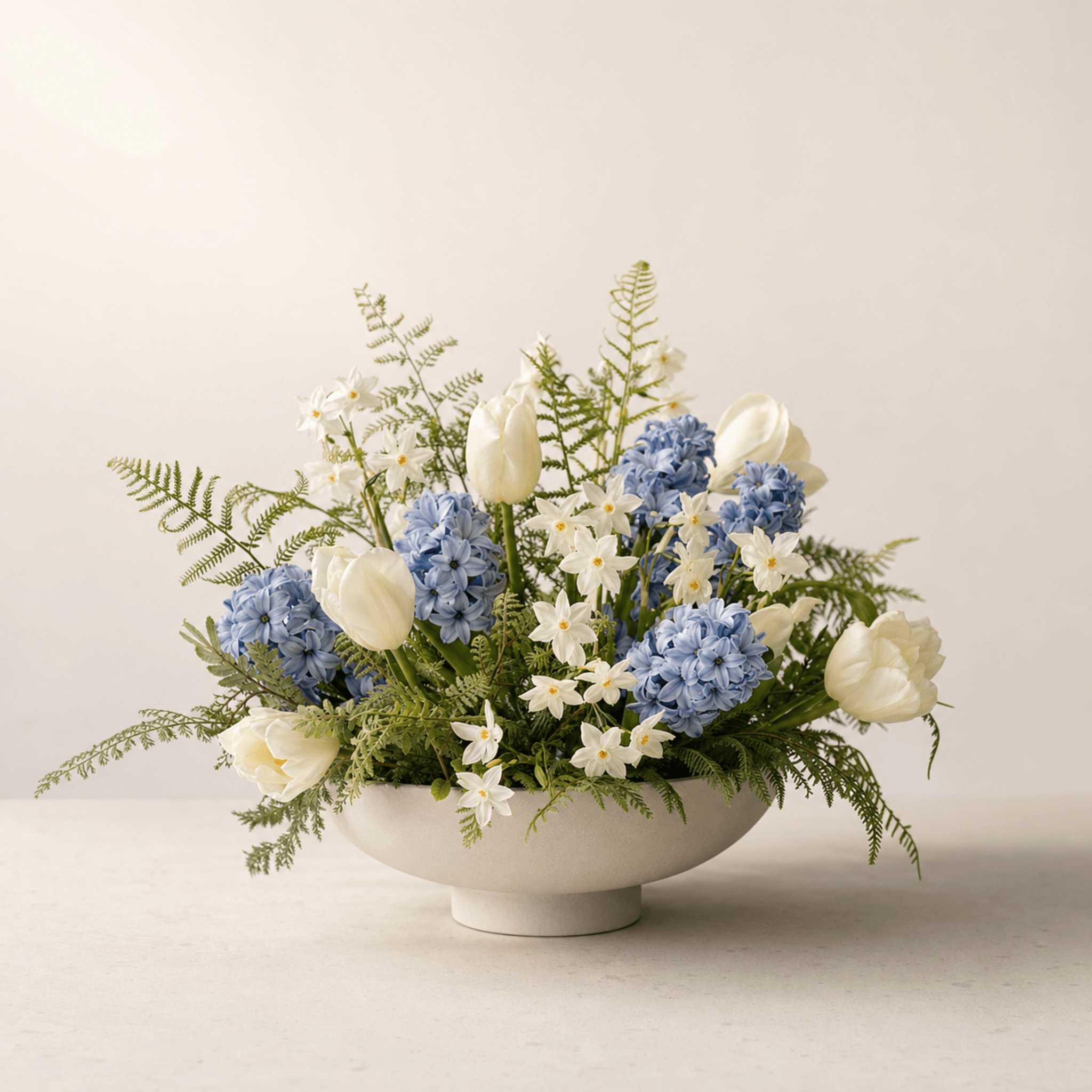 White tulips, blue hyacinths, and white narcissus with ferns in a cream footed ceramic bowl