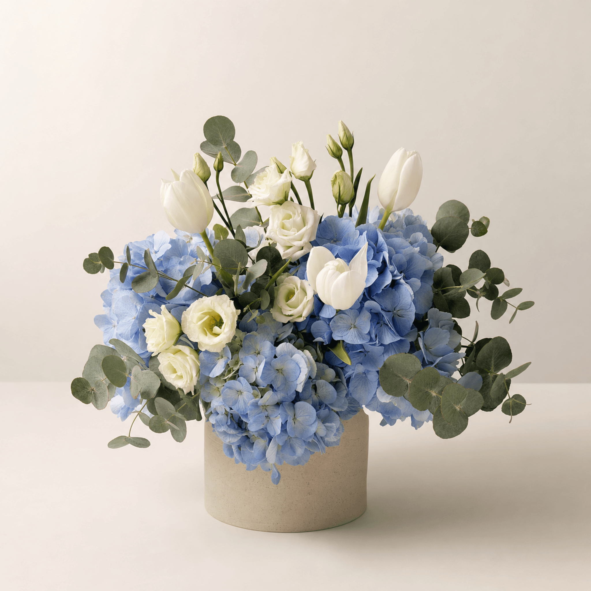 Blue hydrangeas, white tulips, lisianthus and eucalyptus in a stone cylinder vase