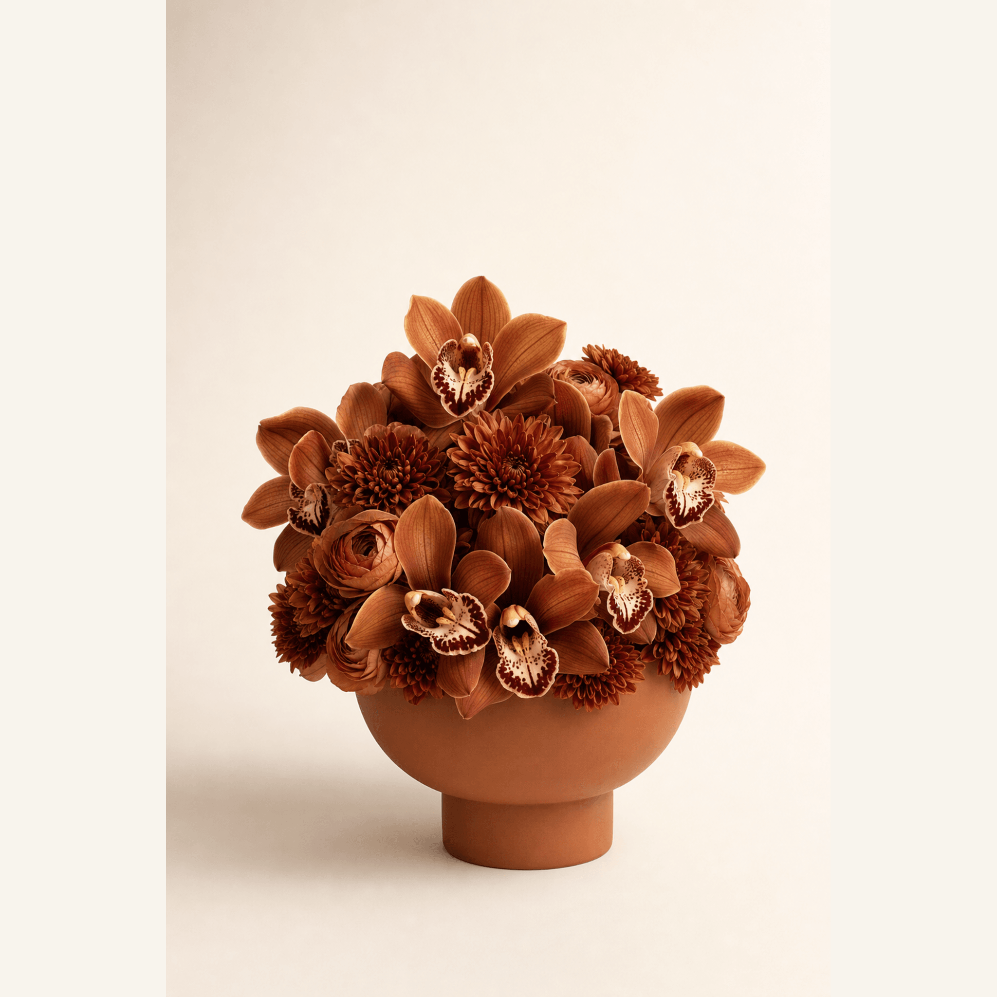 Burnt orange cymbidium orchids, ranunculus, and chrysanthemums in a terracotta footed bowl