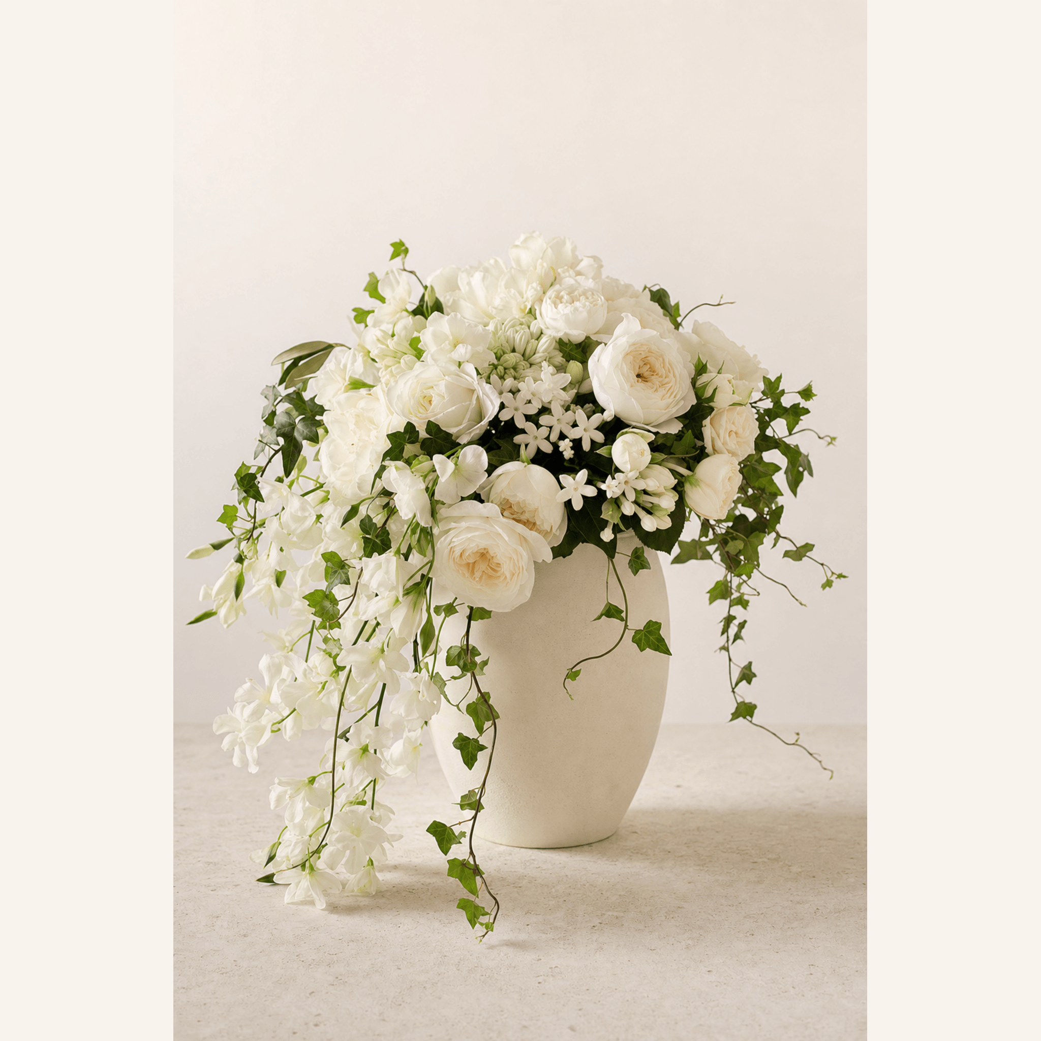 White garden roses, peonies, jasmine, and trailing ivy in a cream ceramic vase