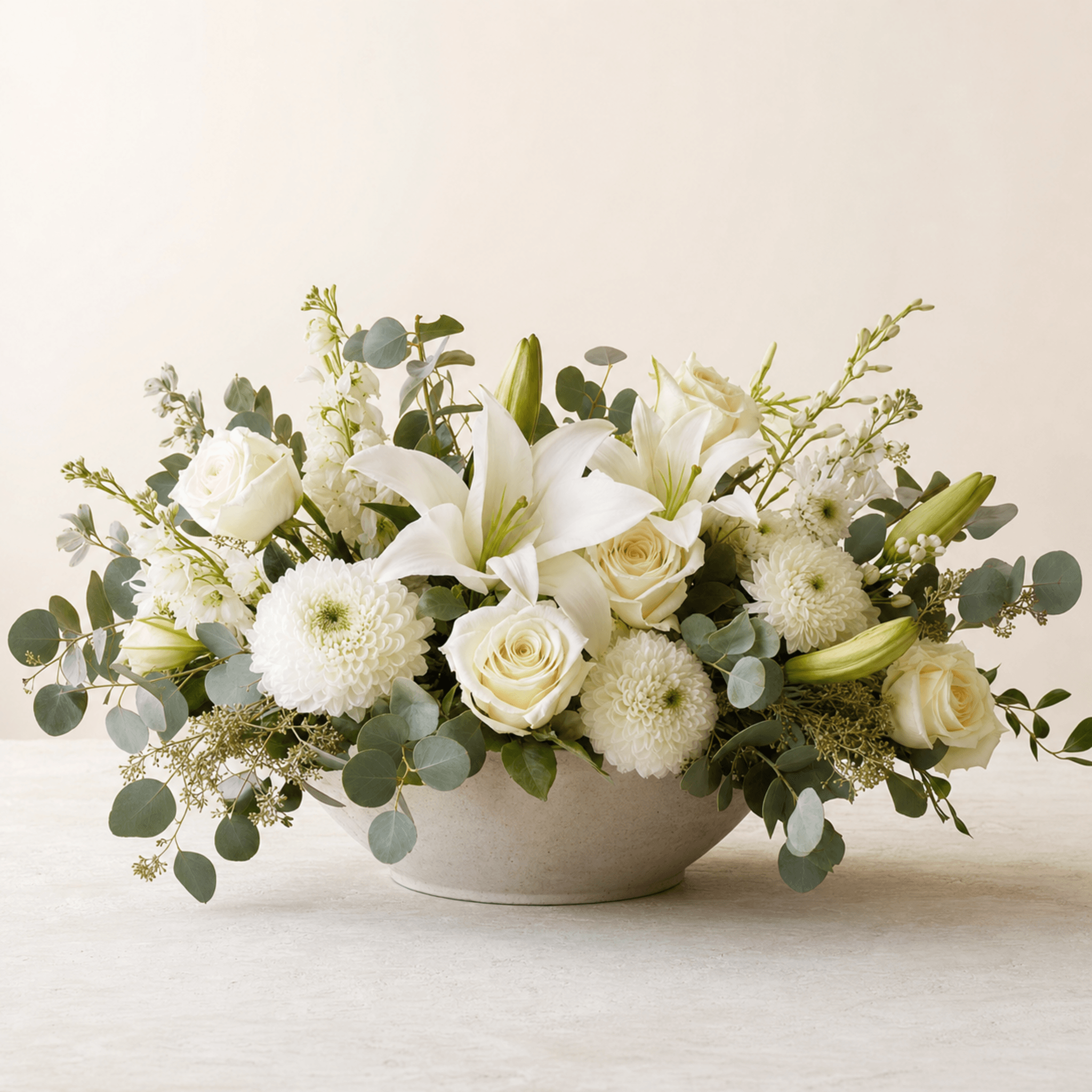 White lilies, roses, chrysanthemums, and eucalyptus in a low ceramic bowl