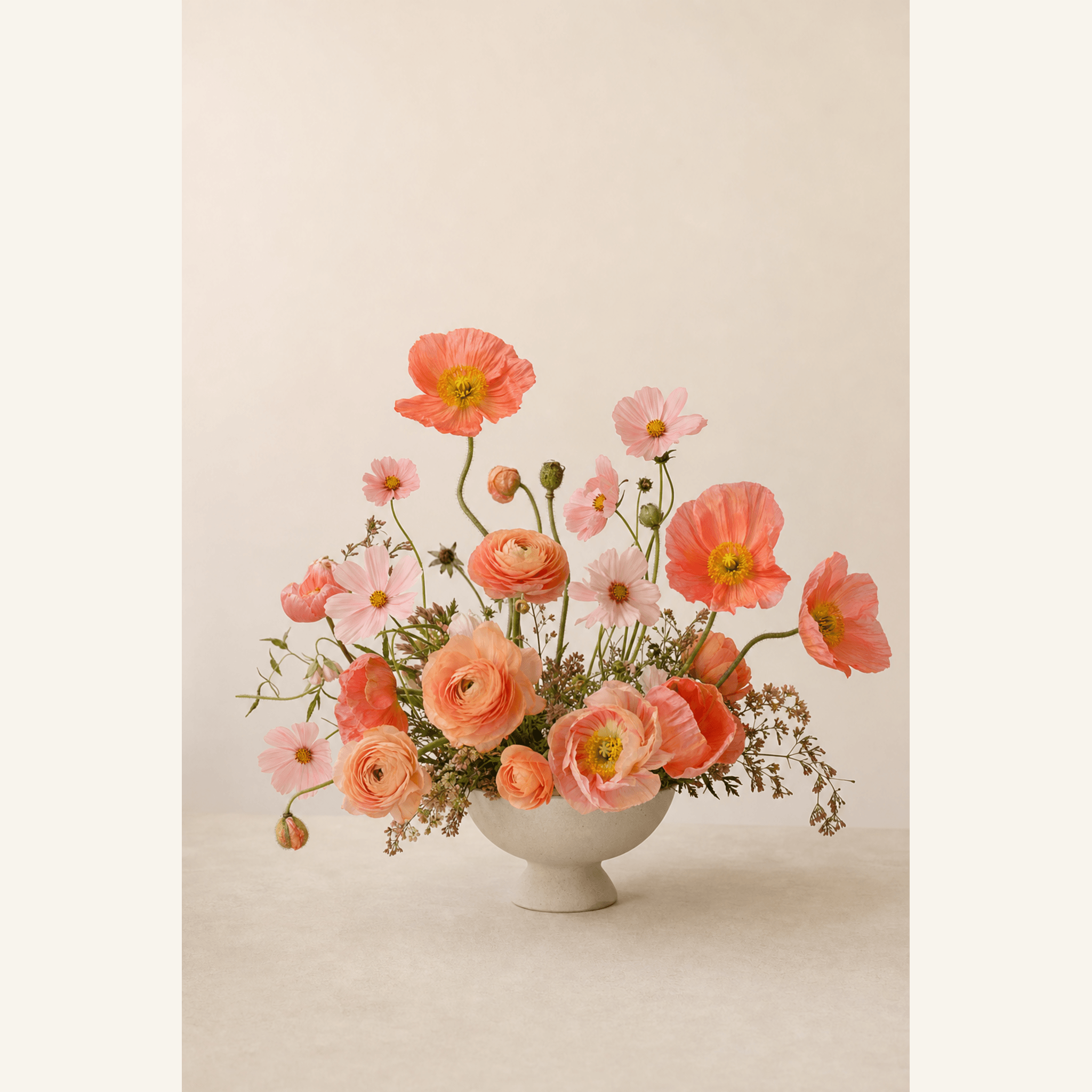 Coral poppies, peach ranunculus, and pink cosmos in a white footed ceramic bowl