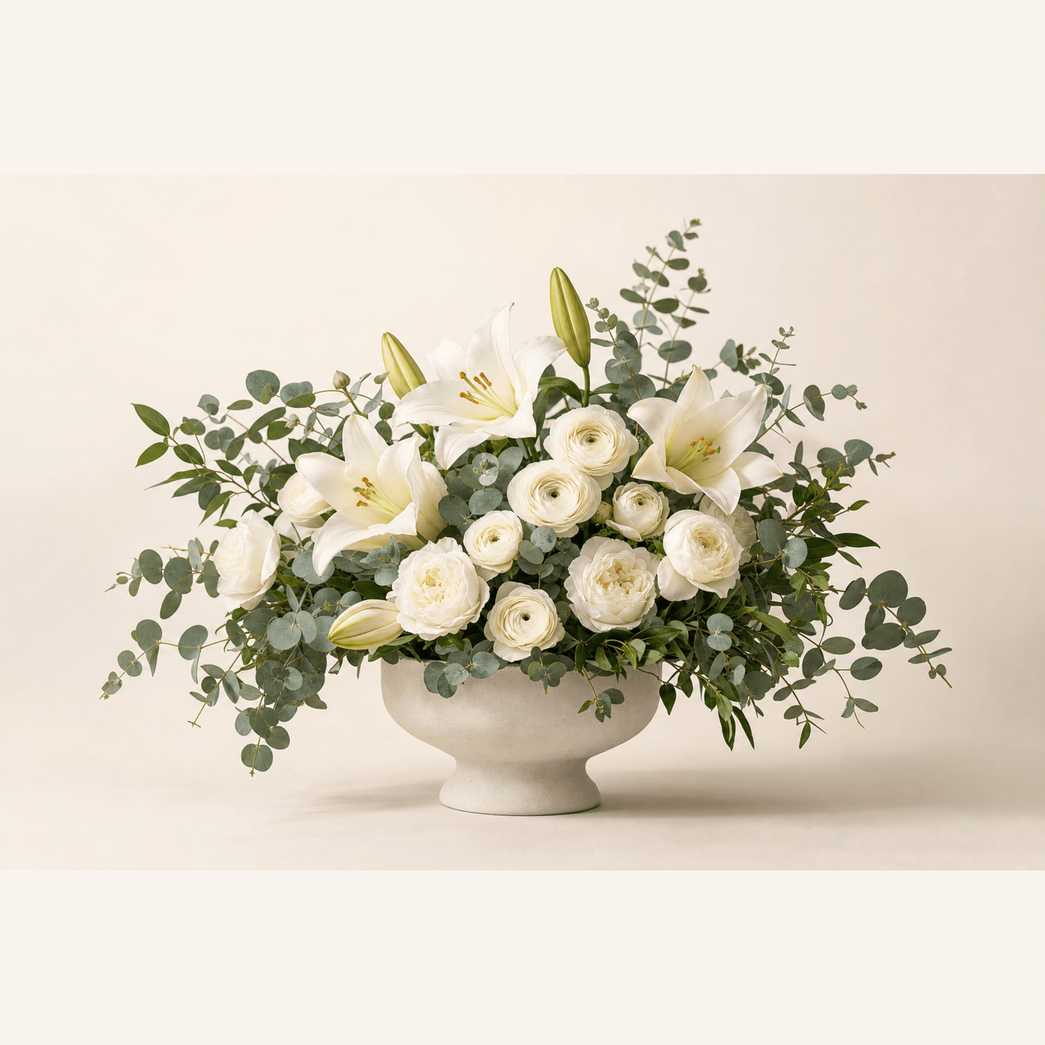White lilies, ranunculus, garden roses, and eucalyptus in a white footed bowl vase
