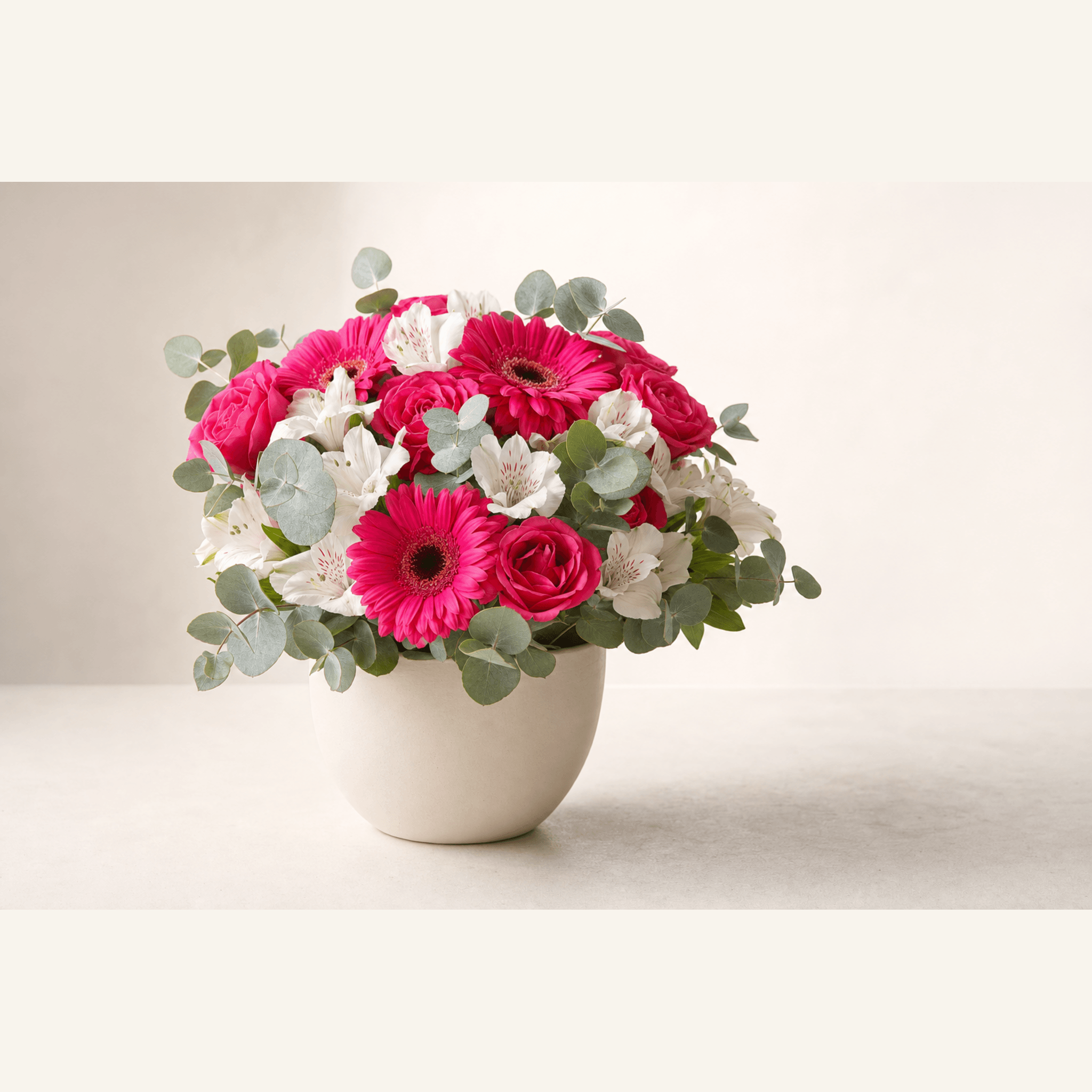 Hot pink gerberas, roses, and white alstroemeria with eucalyptus in a cream ceramic bowl