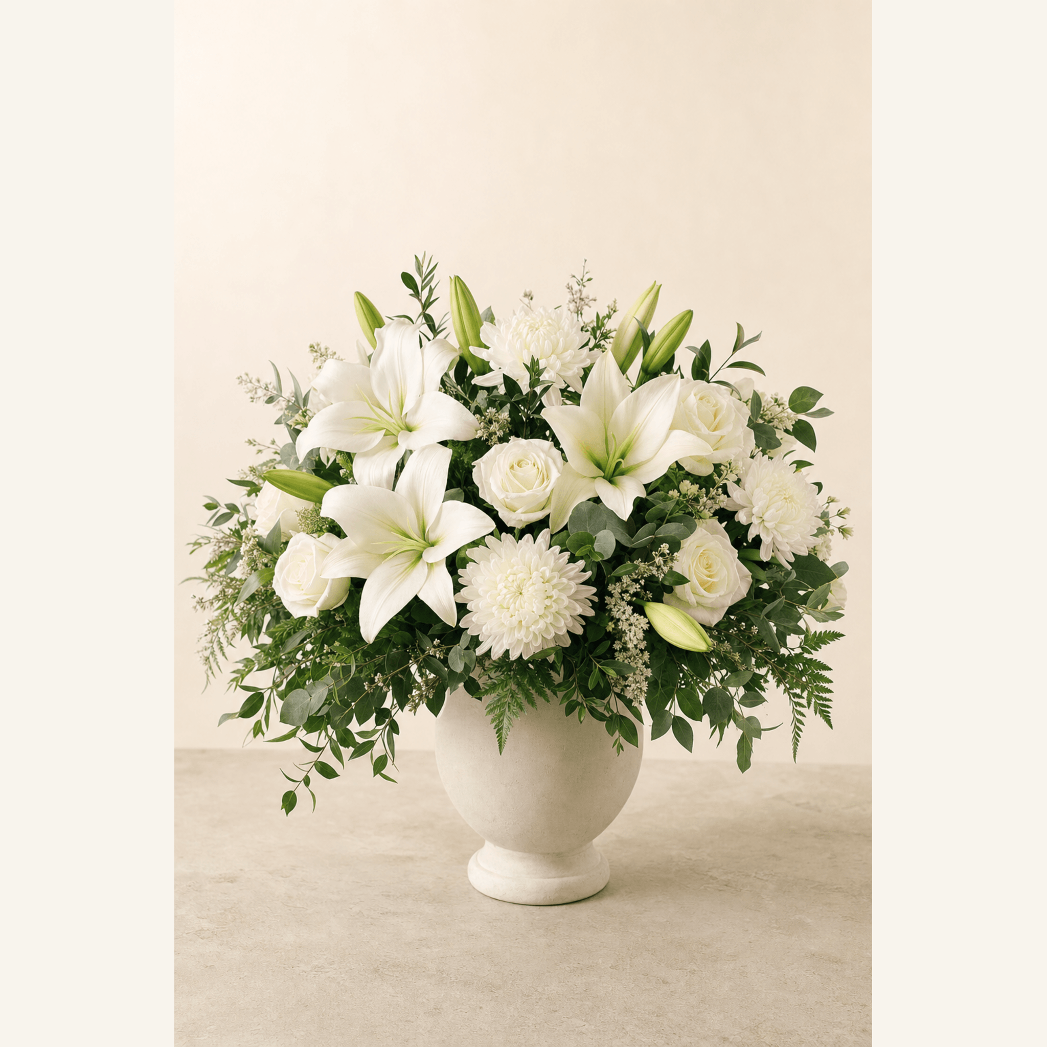White lilies, roses, and chrysanthemums with greenery in a cream ceramic footed vase