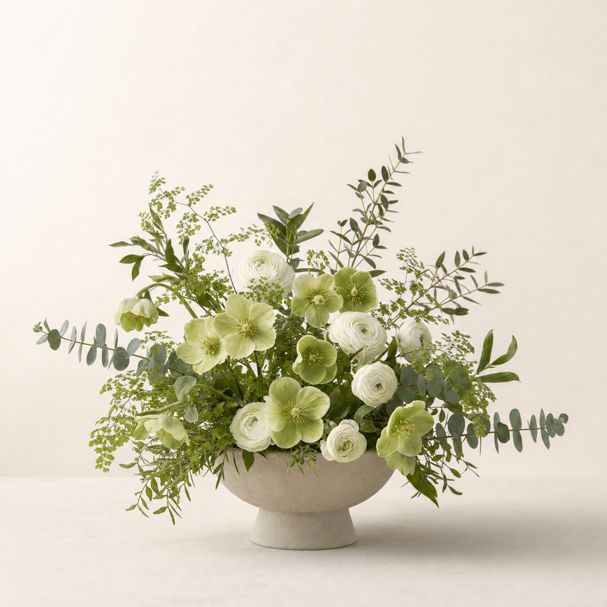 White ranunculus and green hellebores with eucalyptus in a stone footed bowl