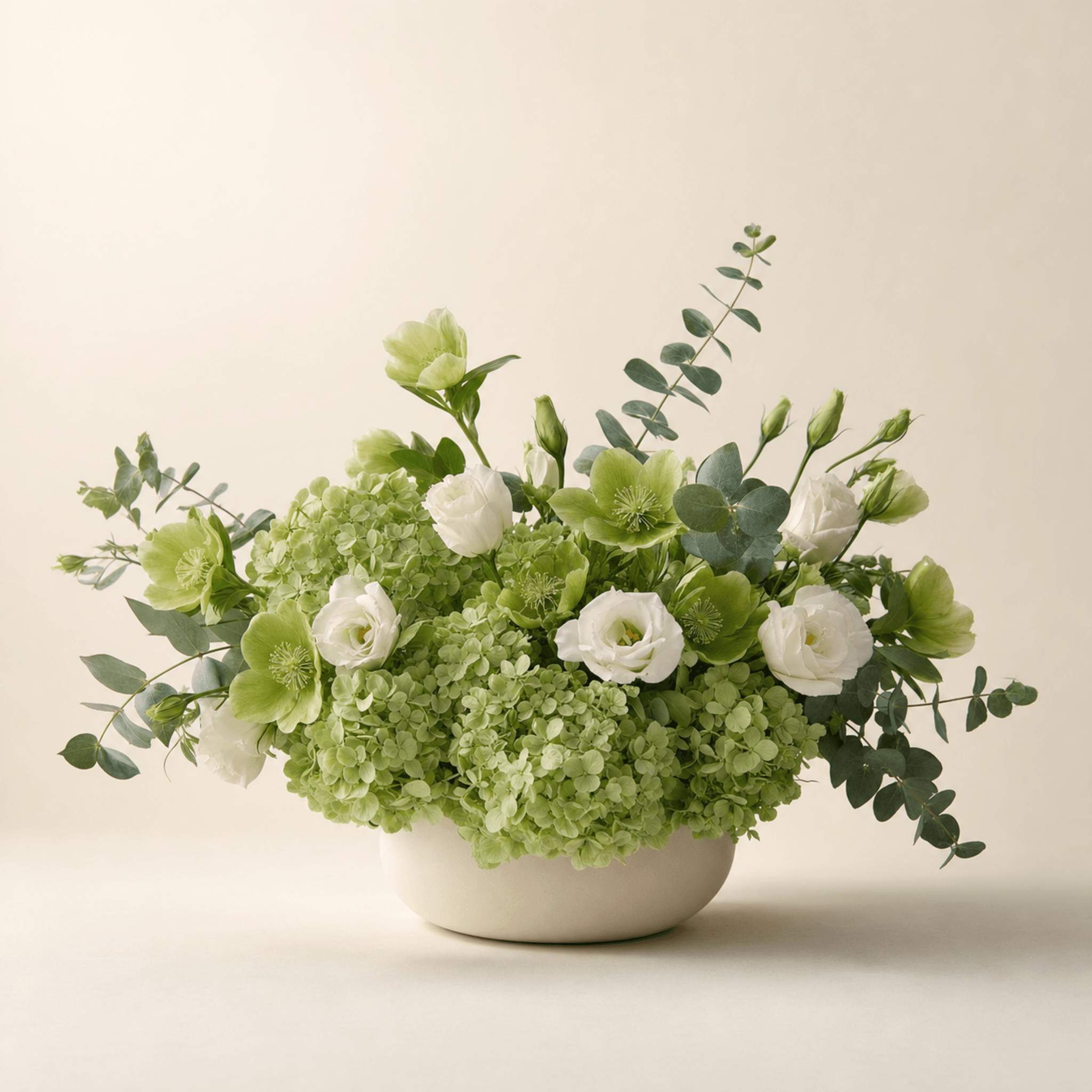 Green hydrangea, white lisianthus, hellebores, and eucalyptus in a low cream ceramic bowl