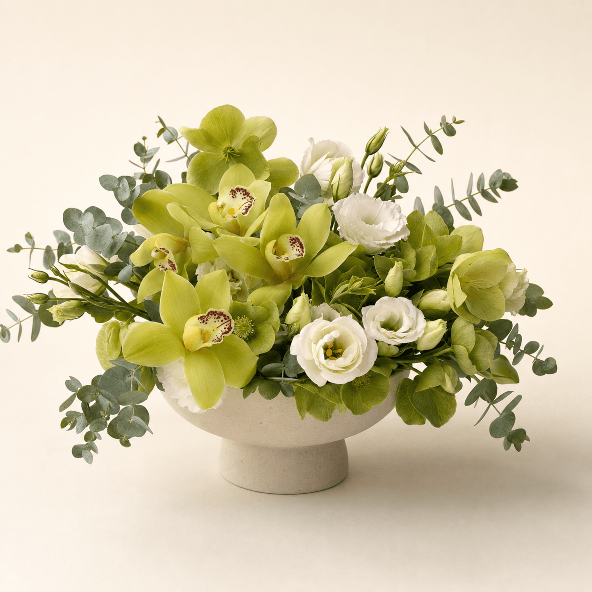 Green cymbidium orchids, white lisianthus, hellebores, and eucalyptus in a footed ceramic bowl