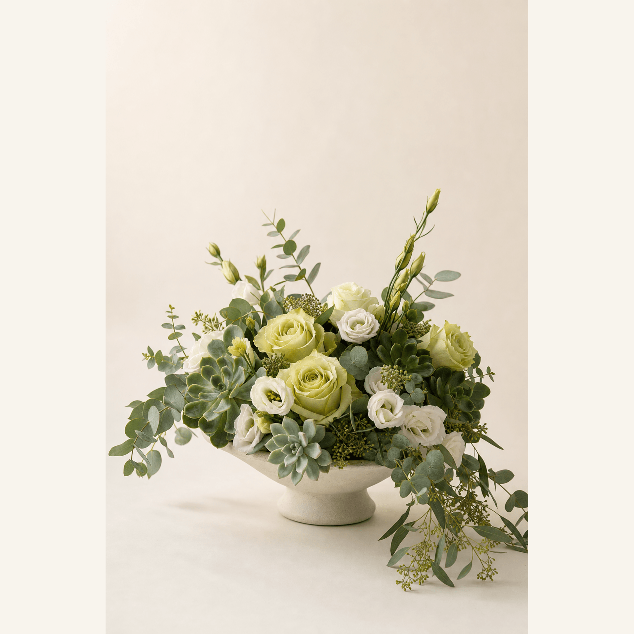 White and green roses, lisianthus, succulents, and eucalyptus in a footed ceramic bowl
