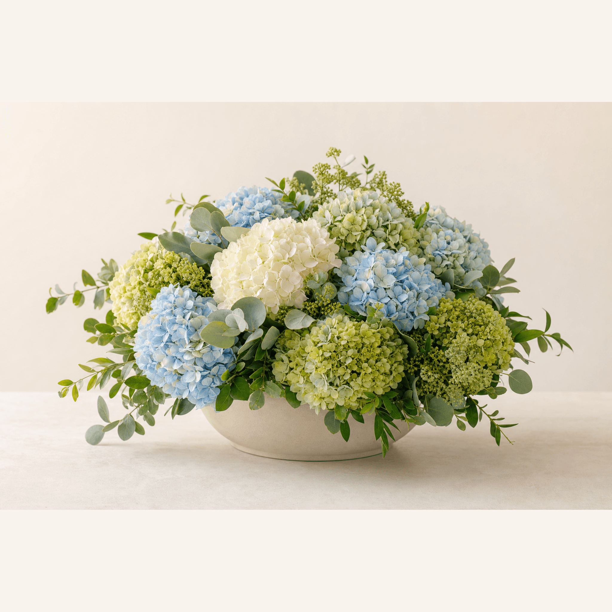 Blue, white, and green hydrangeas with eucalyptus in a low white ceramic bowl