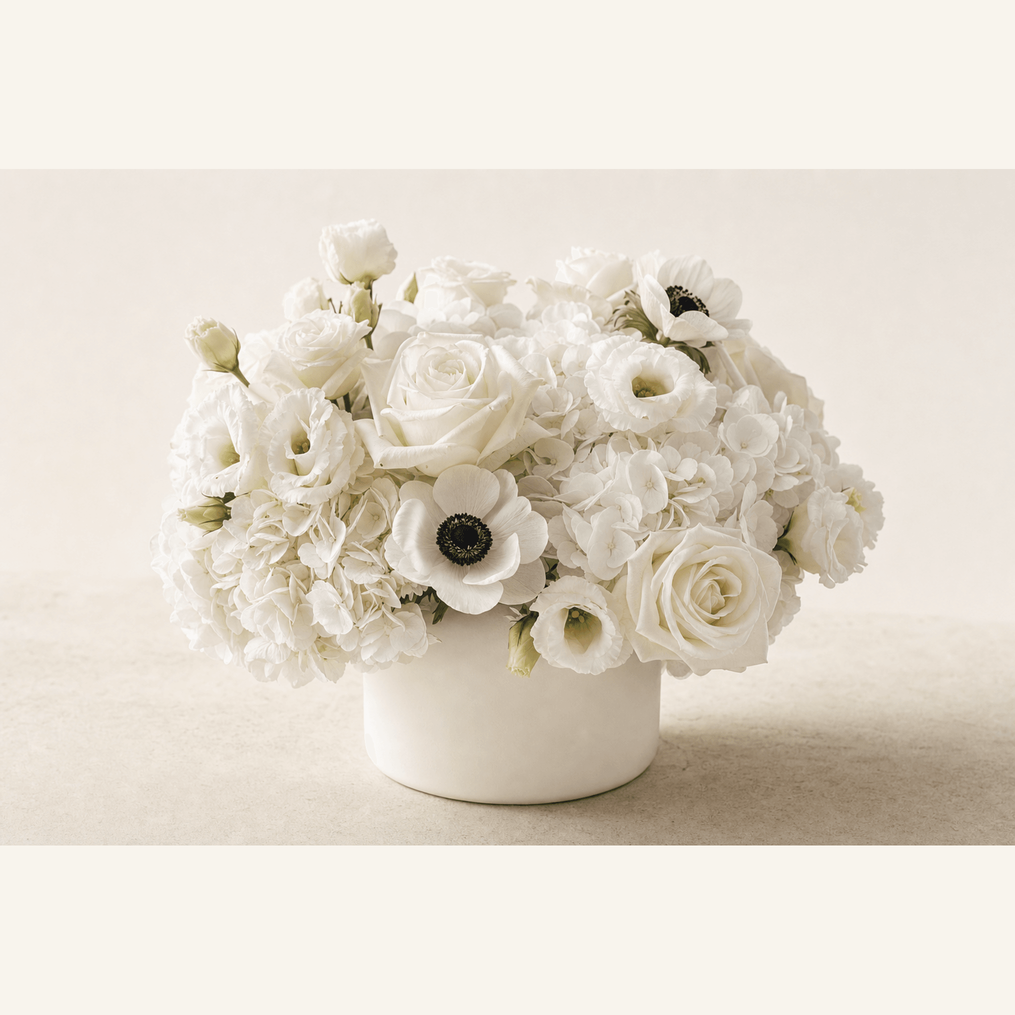White hydrangea, roses, lisianthus, and anemones arranged in a low white ceramic bowl