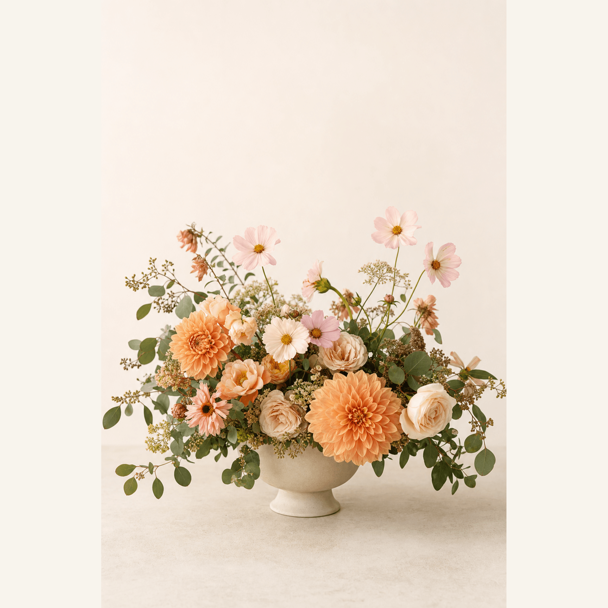 Peach dahlias, cream roses, pink cosmos, and eucalyptus in a wide footed ceramic bowl