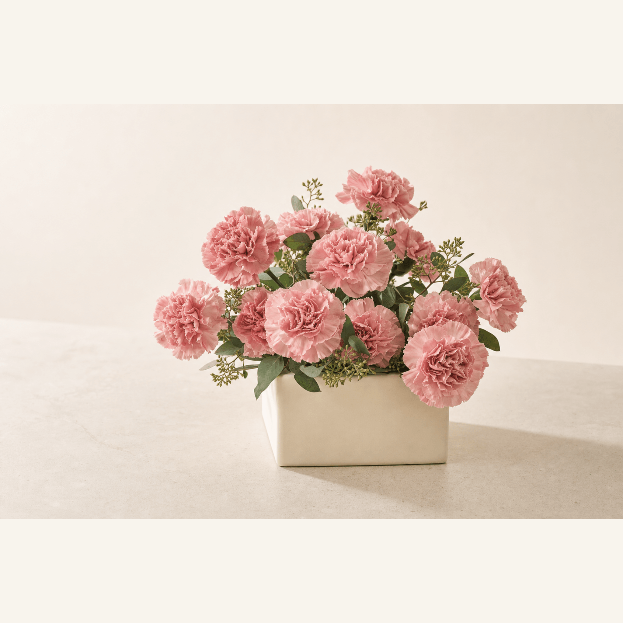 Pink carnations with eucalyptus foliage arranged in a rectangular cream ceramic vase