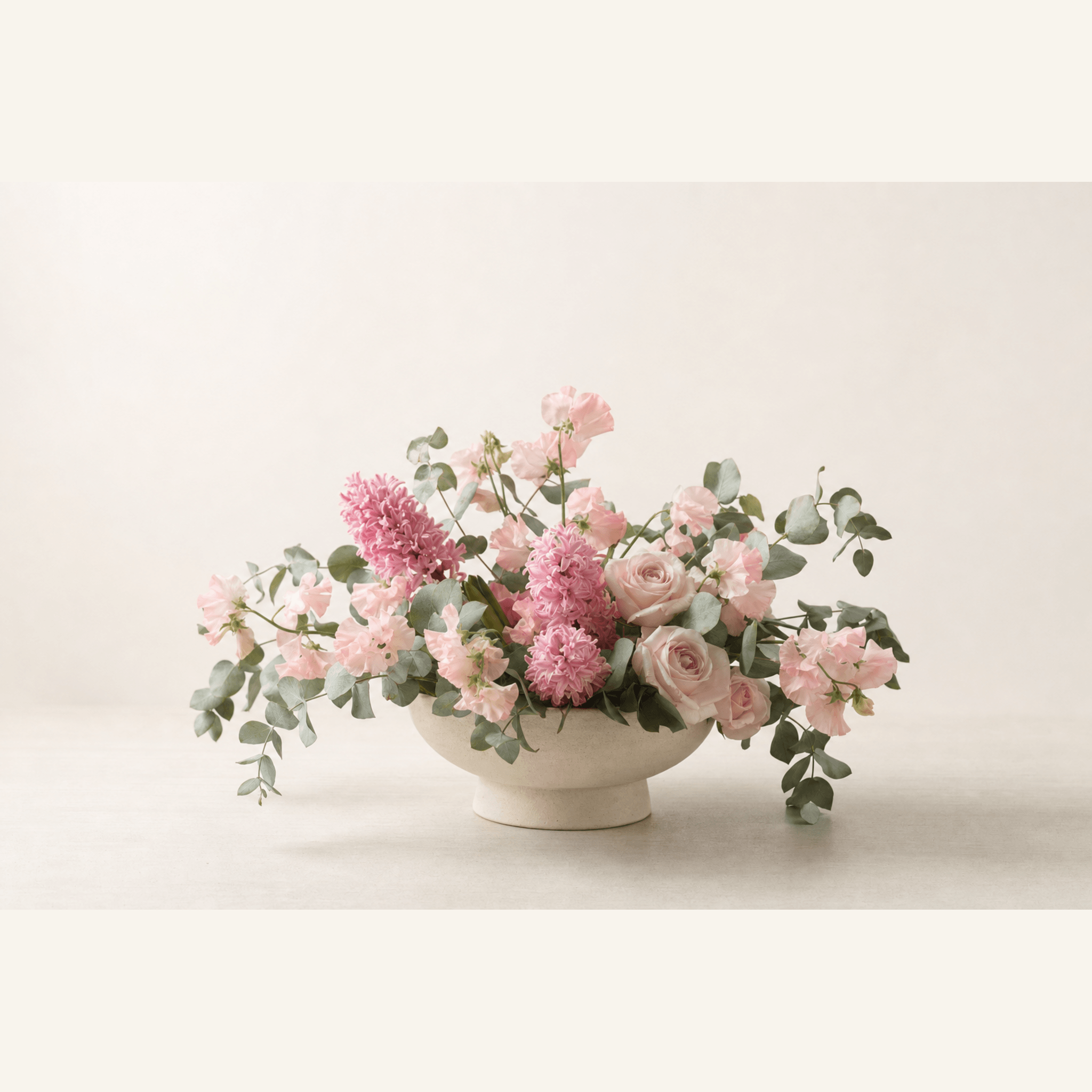 Pink hyacinths, roses, sweet peas, and eucalyptus in a white footed ceramic bowl
