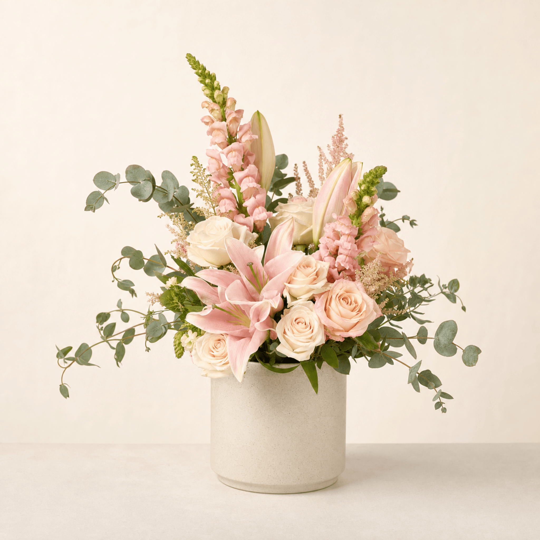 Blush roses, pink oriental lilies, snapdragons, astilbe and eucalyptus in a white ceramic cylinder vase