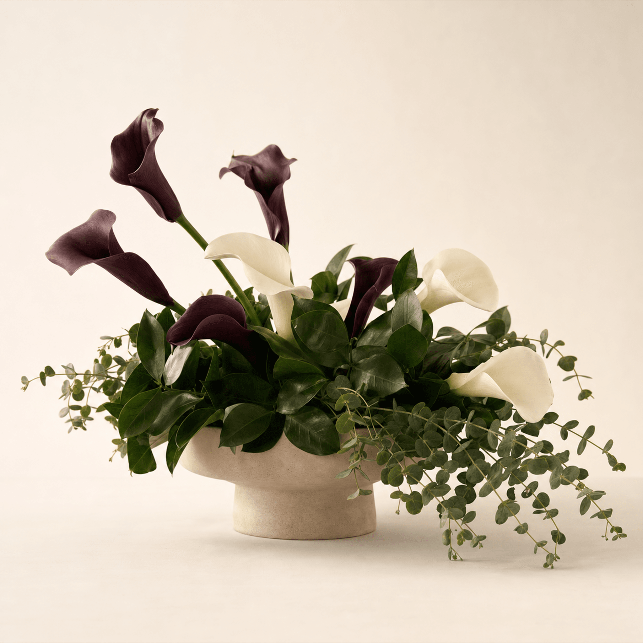 Deep burgundy and white calla lilies with eucalyptus in a low stone pedestal bowl