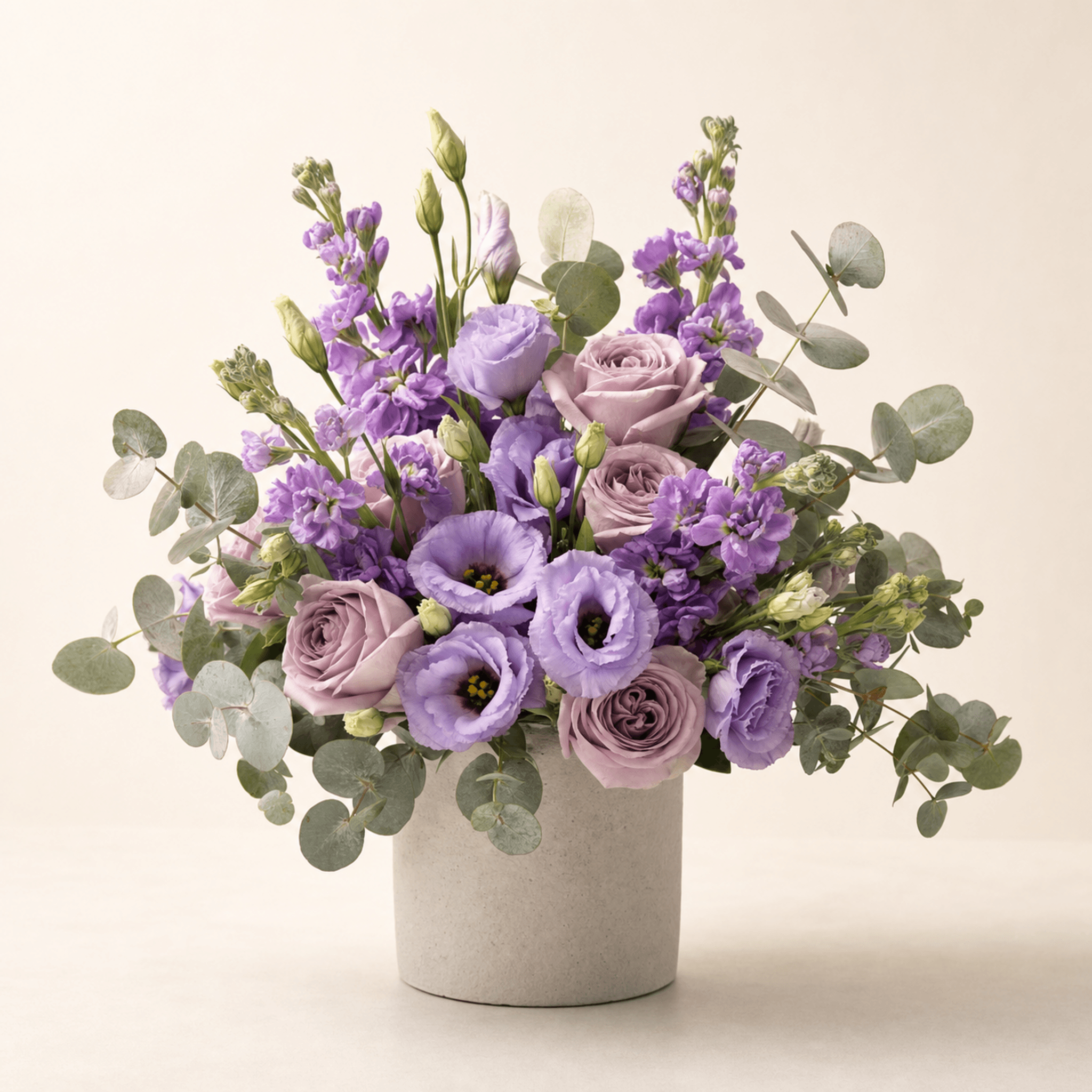 Lavender roses, lisianthus, stock flowers, and eucalyptus in a cylindrical stone pot