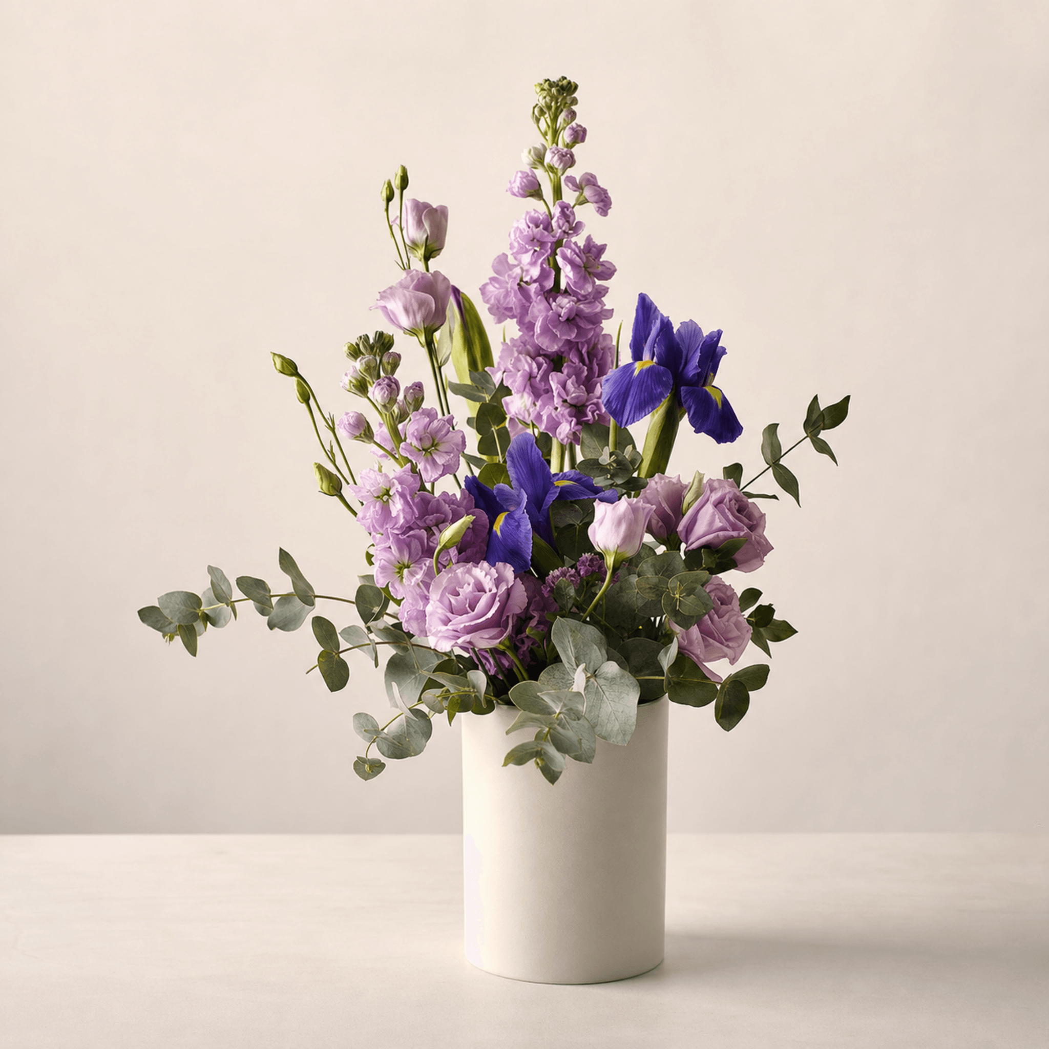 Lavender lisianthus, stock, blue iris and eucalyptus in a white ceramic cylinder vase