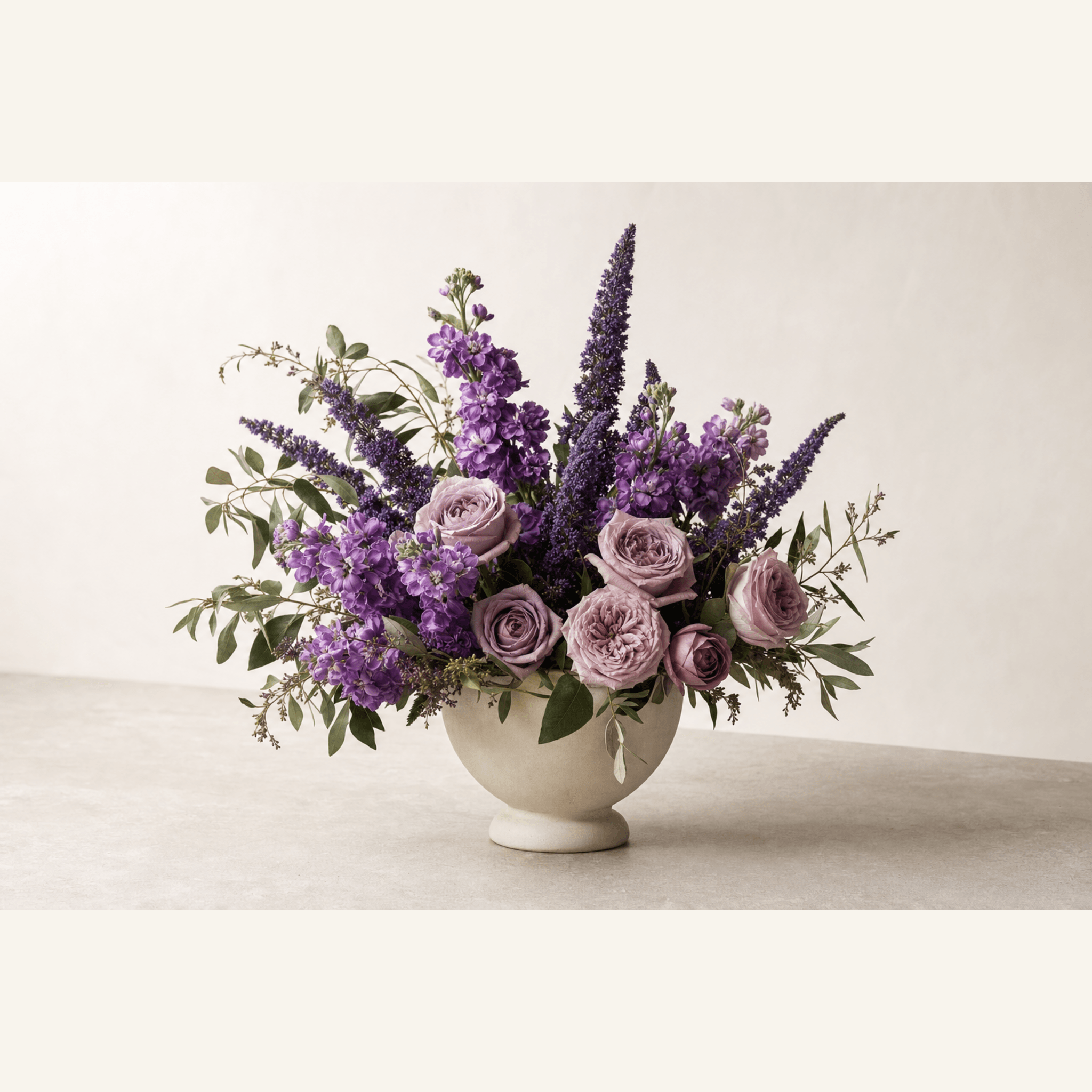 Lavender roses, purple stock, veronica spikes and eucalyptus in a cream footed bowl