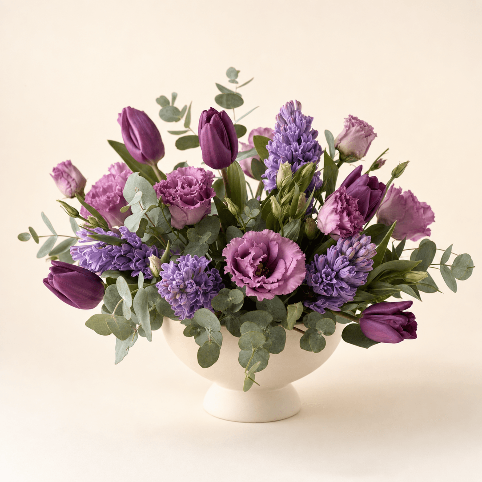 Purple tulips, hyacinths, lisianthus, and eucalyptus in a white footed ceramic bowl