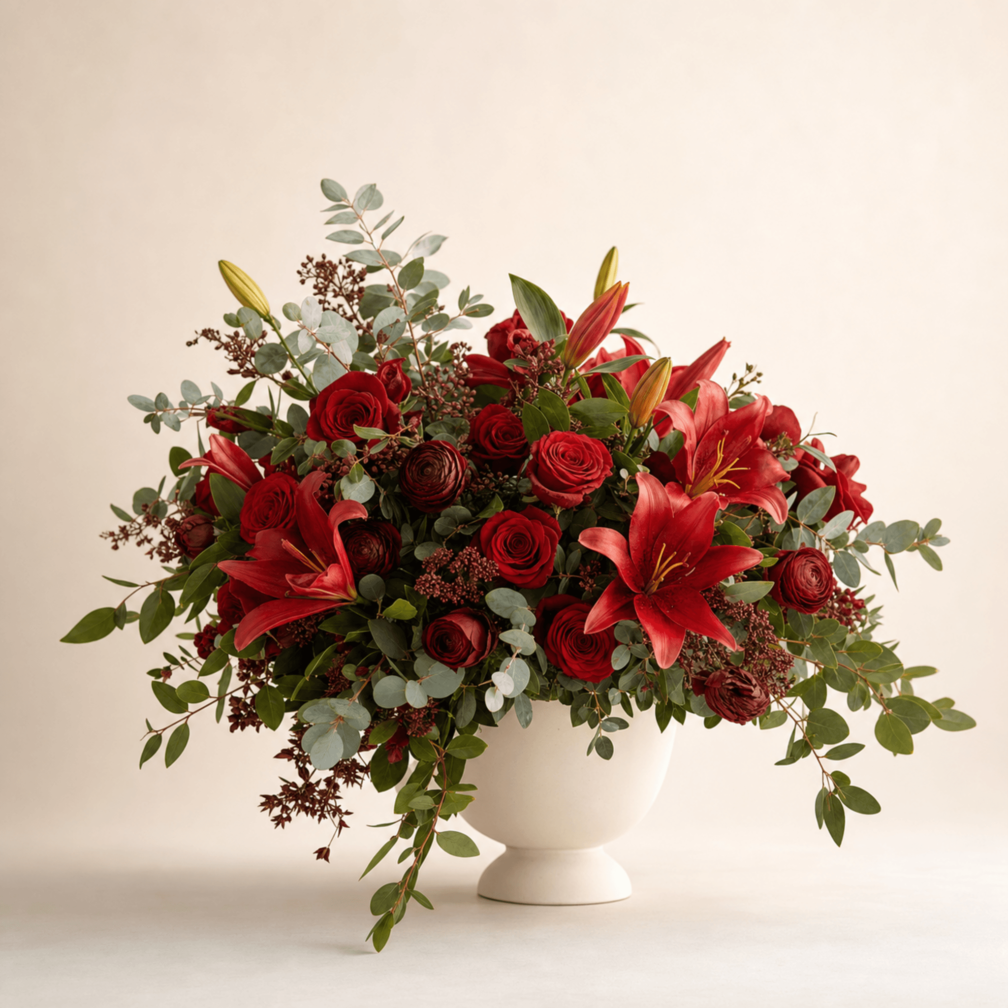 Red roses, ranunculus, oriental lilies, and eucalyptus in a white footed ceramic bowl