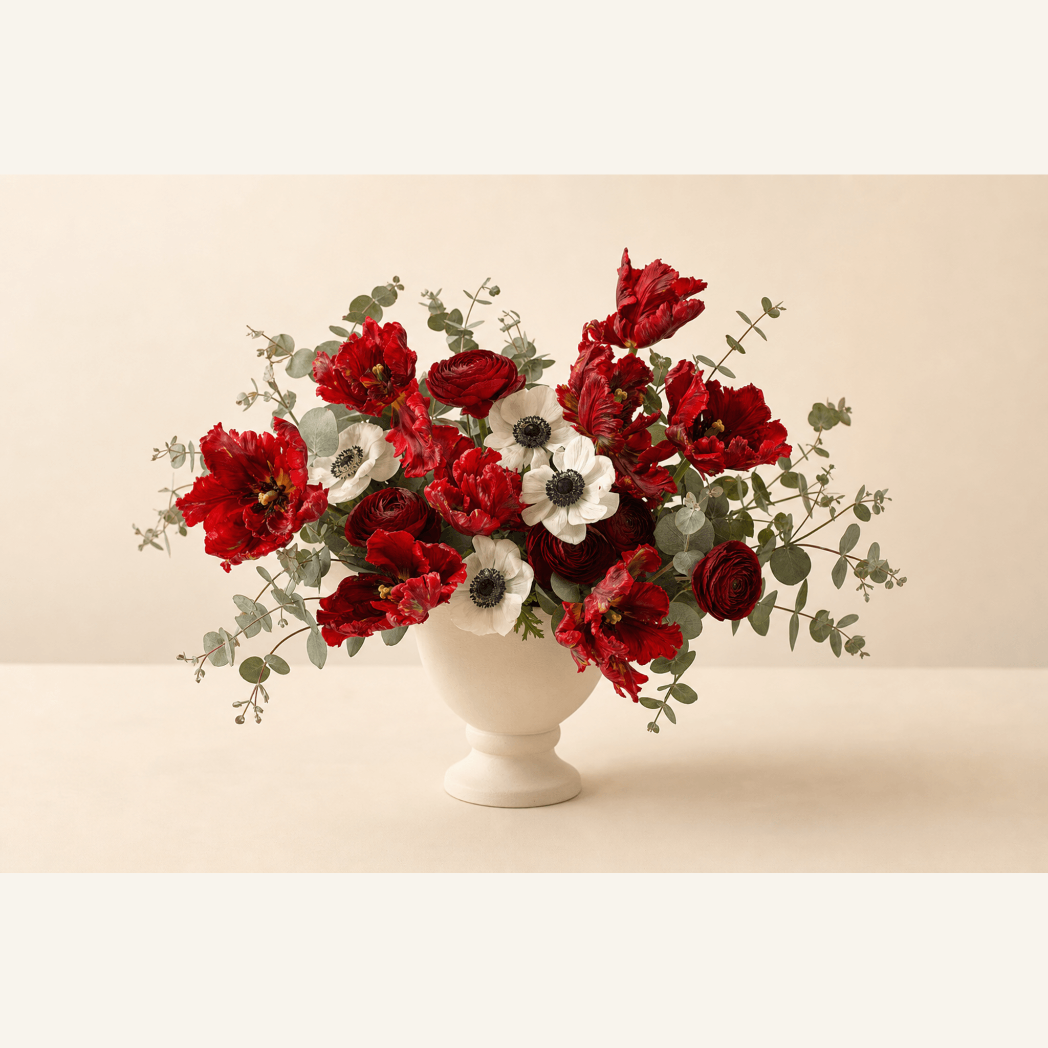 Red parrot tulips, ranunculus, and white anemones with eucalyptus in a white footed bowl