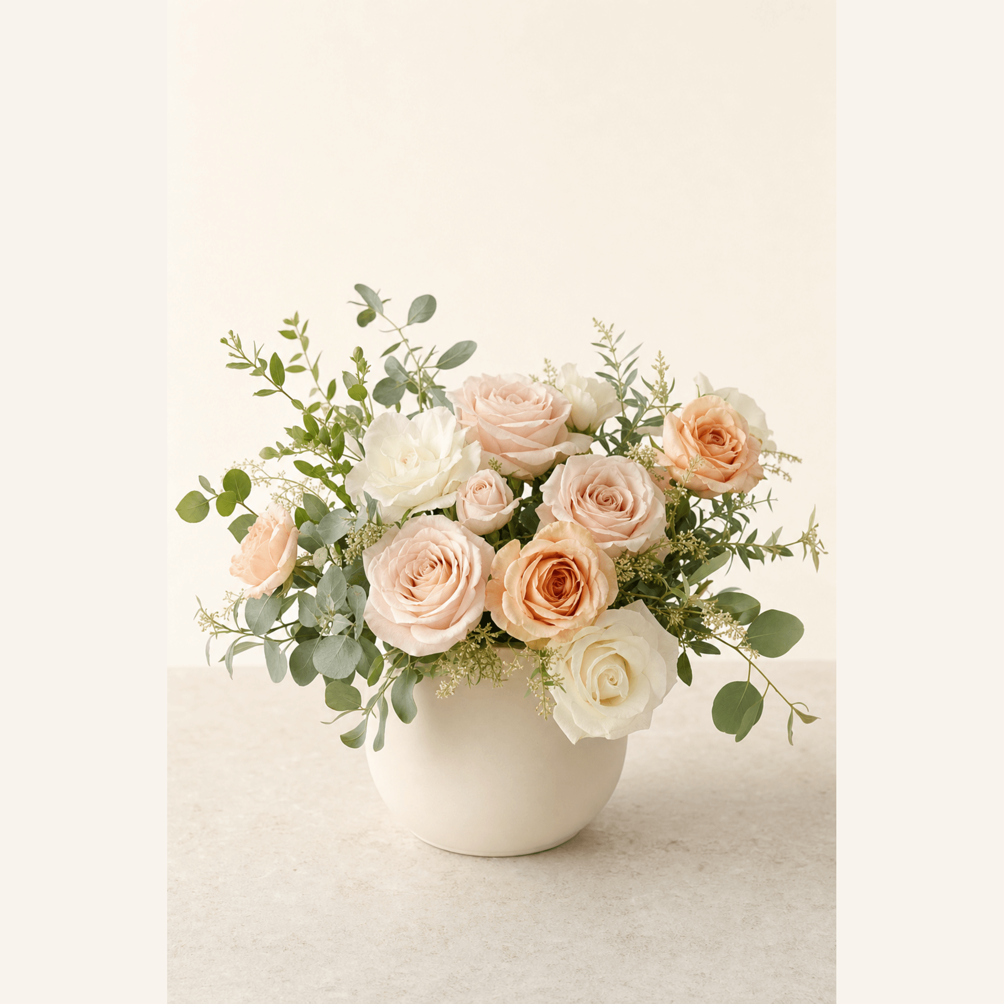 Blush, peach, and white roses with eucalyptus in a round white ceramic vase