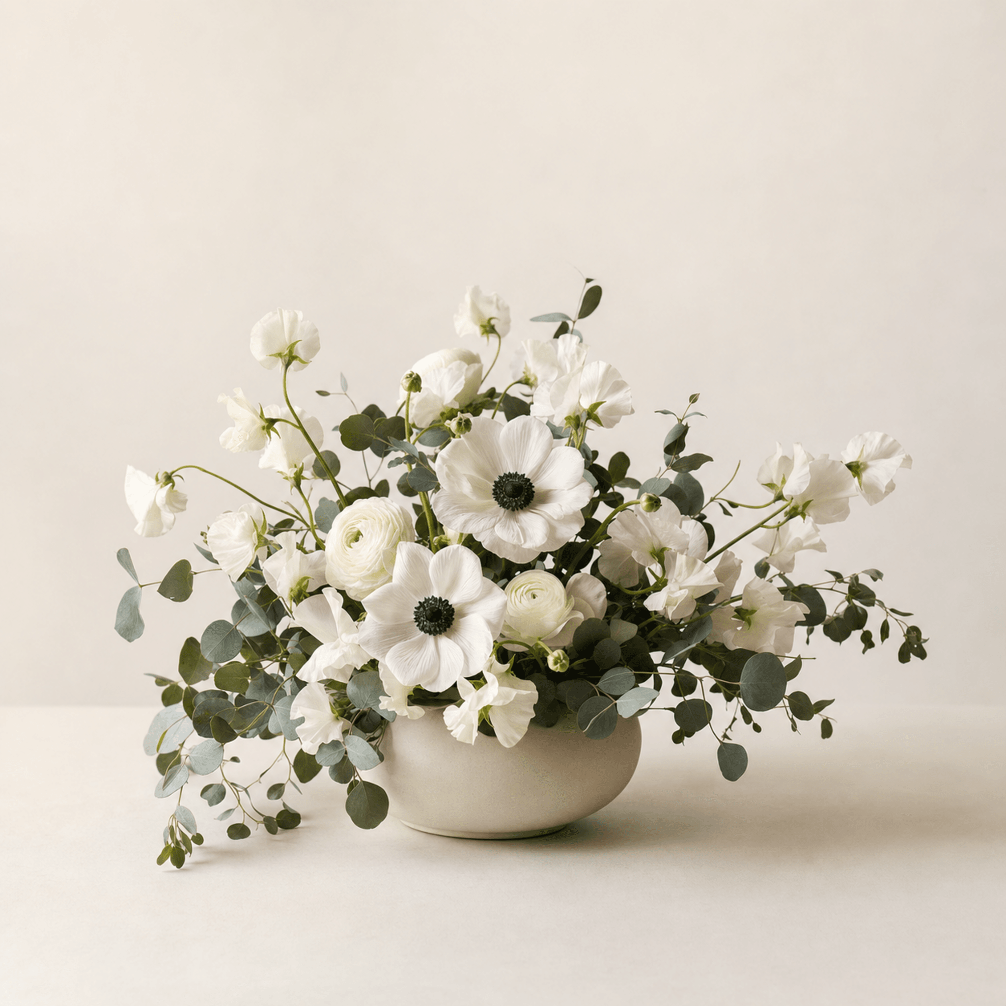 White anemones, ranunculus, sweet peas, and eucalyptus in a low cream ceramic bowl