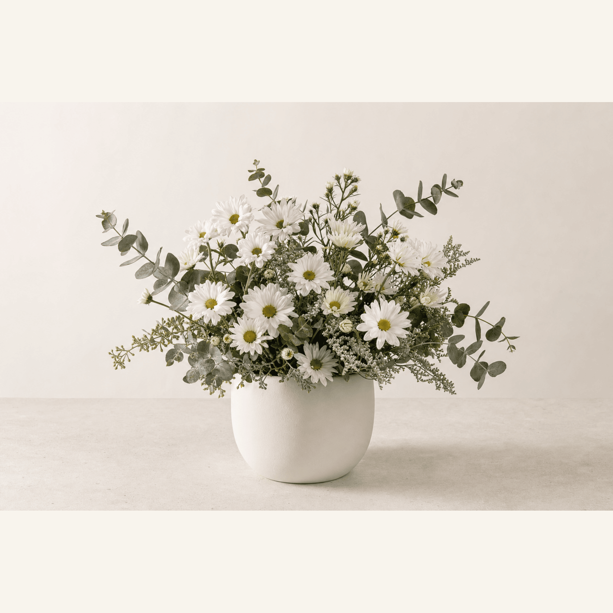 White daisies and eucalyptus in a wide low white ceramic bowl arrangement