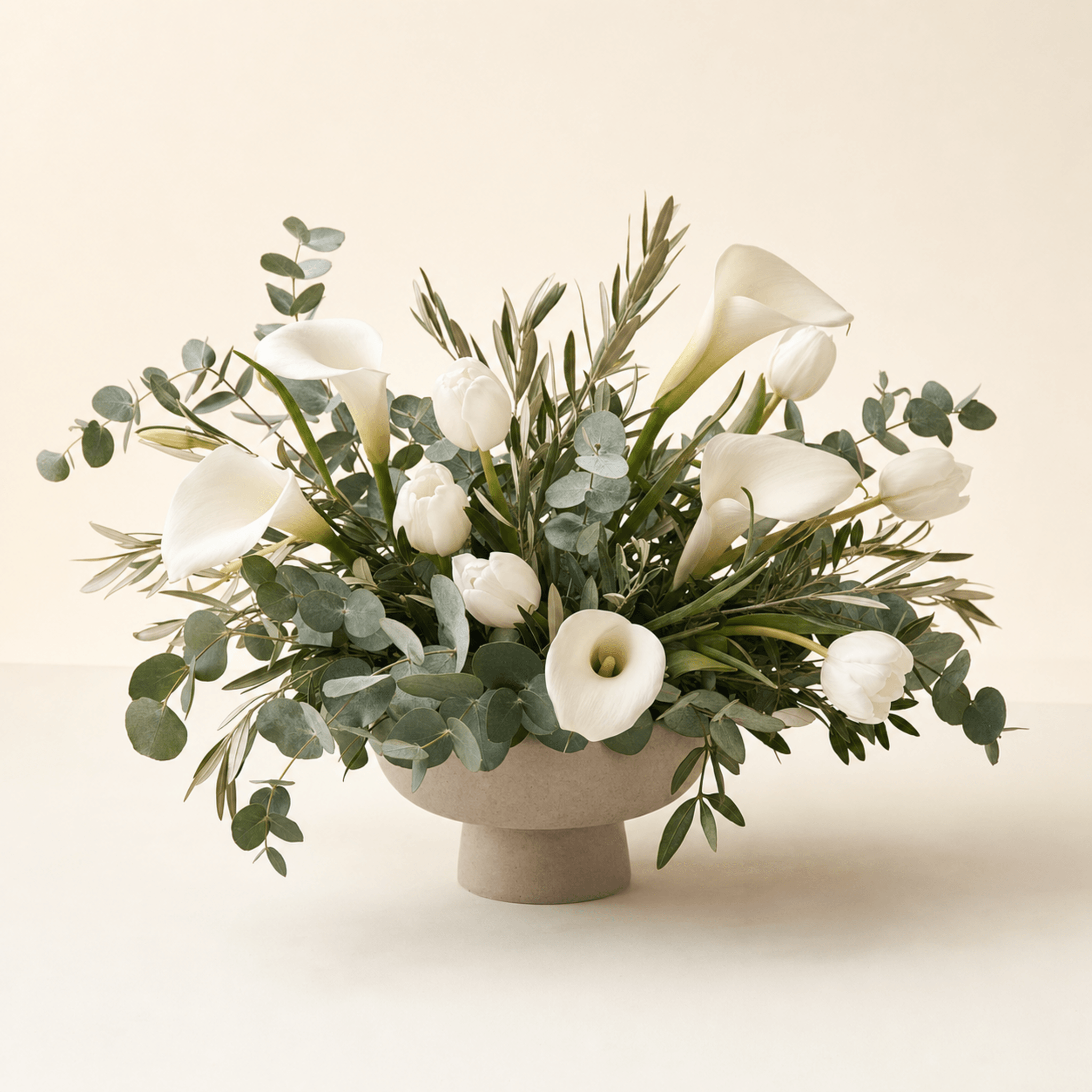 White calla lilies and tulips with eucalyptus in a wide footed ceramic bowl