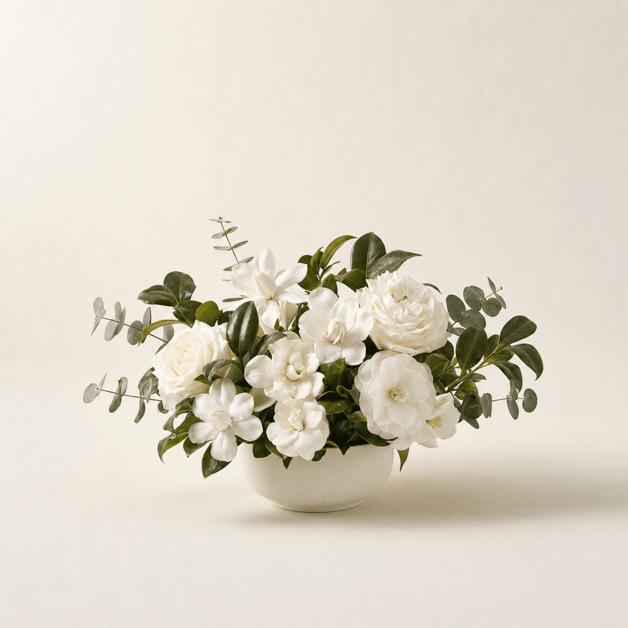 White gardenias, roses, and eucalyptus in a low white ceramic bowl arrangement