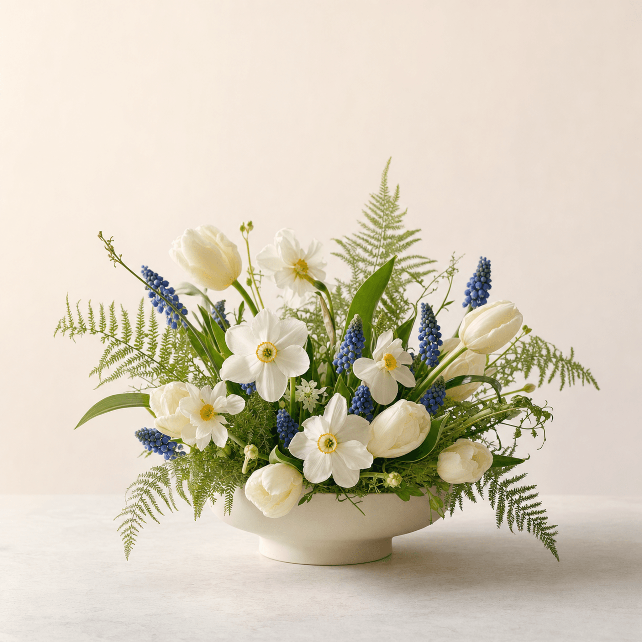 White tulips, narcissi, and blue grape hyacinths with ferns in a cream footed bowl