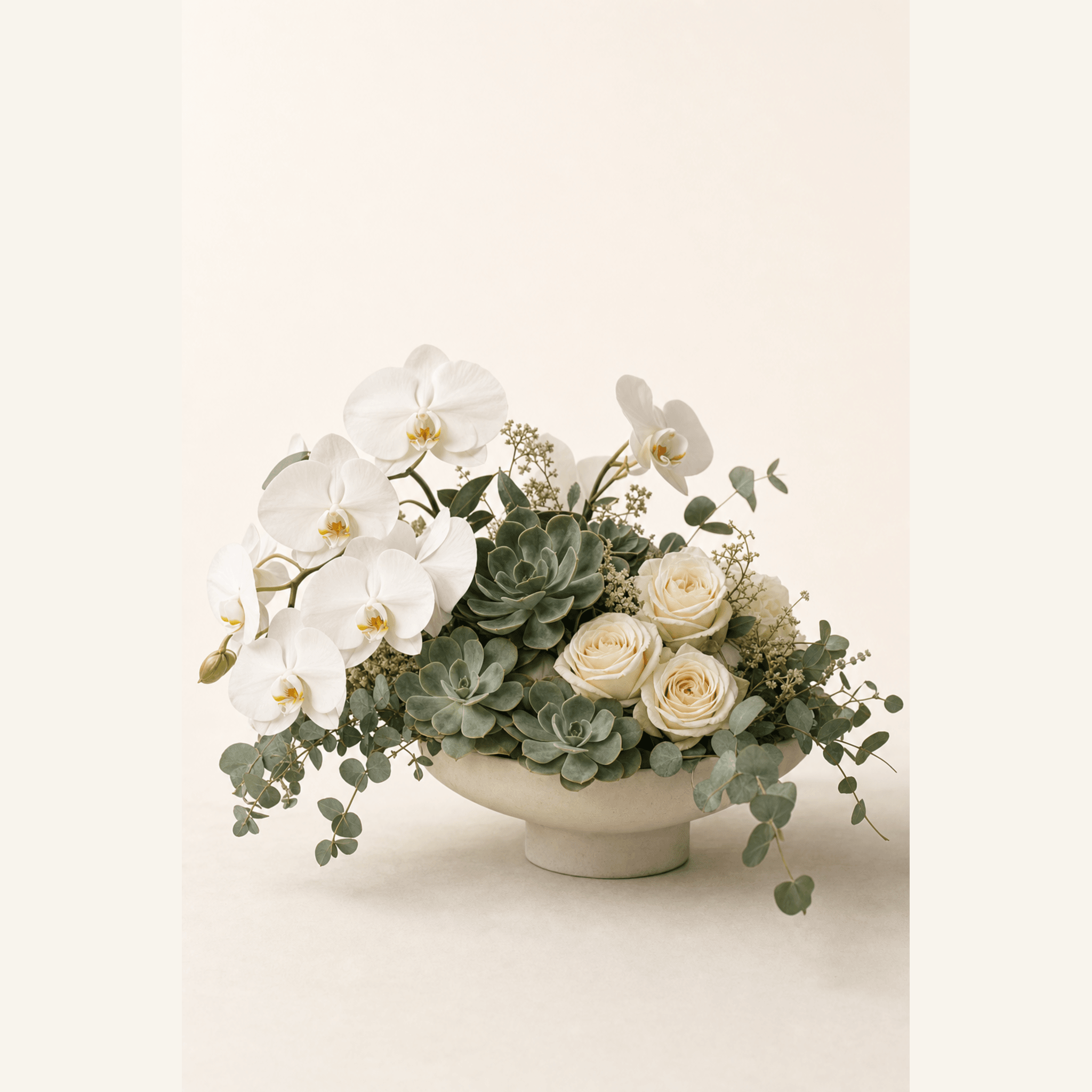 White phalaenopsis orchids, cream roses, succulents, and eucalyptus in a wide footed ceramic bowl