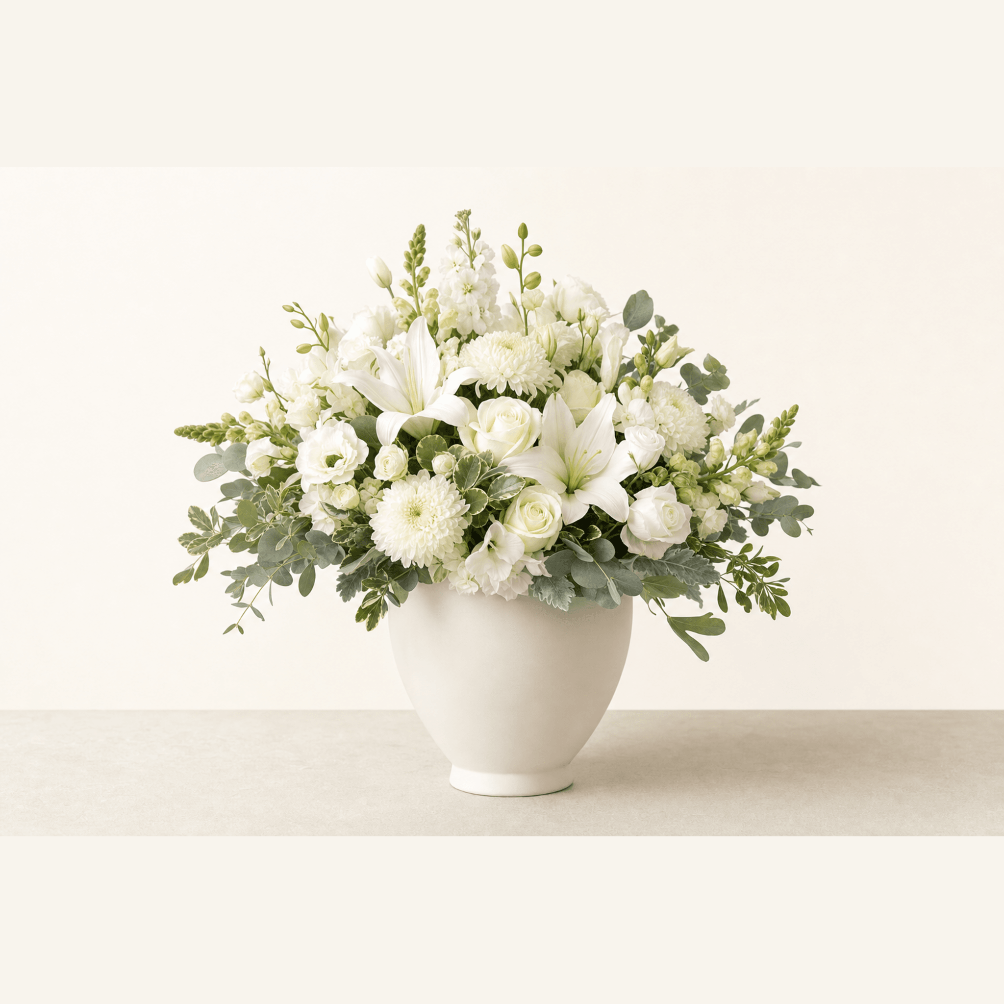 White roses, lilies, chrysanthemums, and lisianthus with eucalyptus in a white ceramic footed bowl