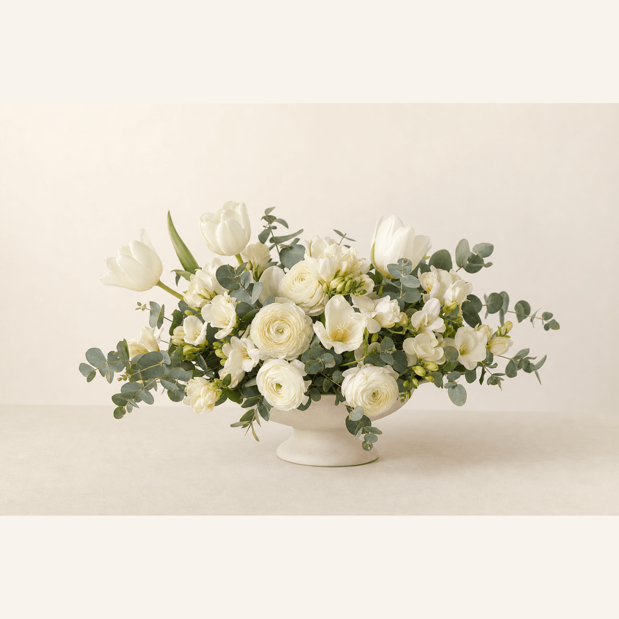 White tulips, ranunculus, freesia, and eucalyptus in a white footed ceramic bowl