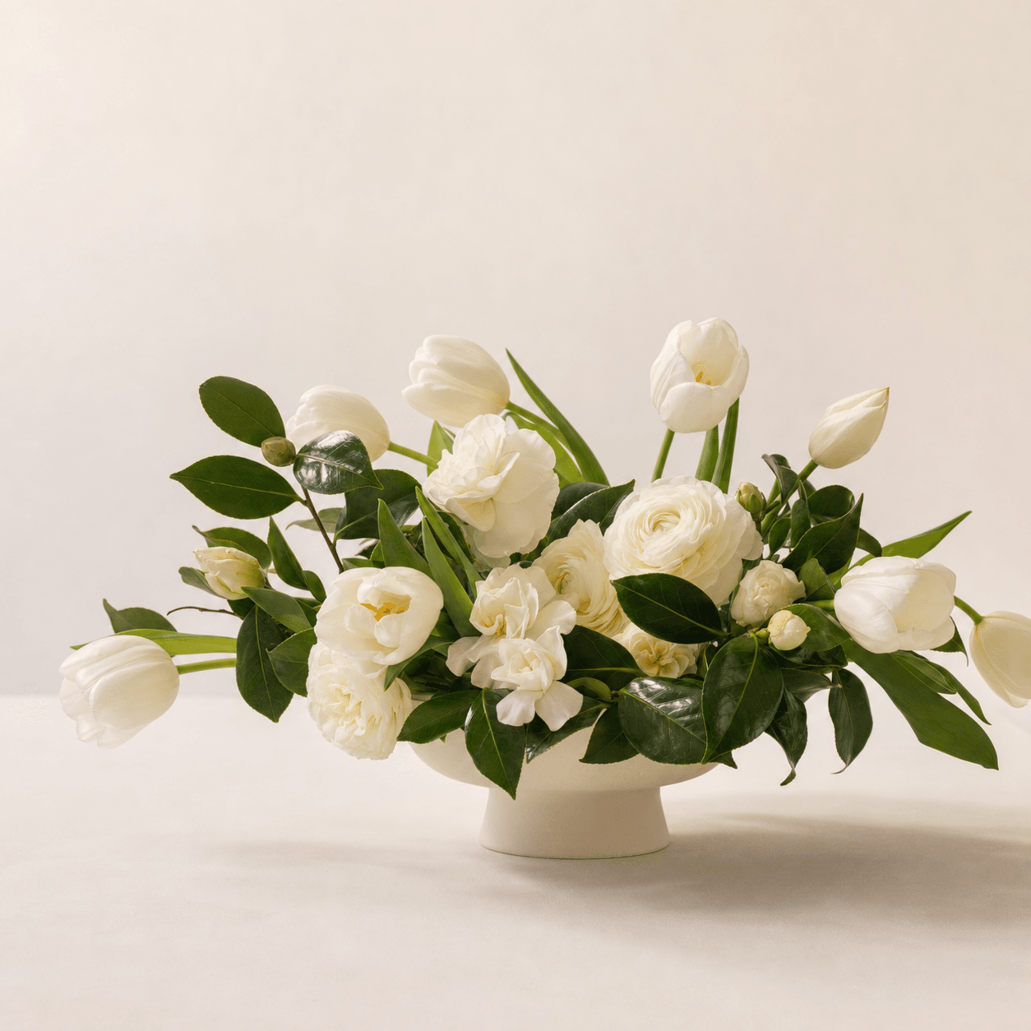 White tulips, ranunculus, garden roses, and gardenia in a white footed ceramic bowl